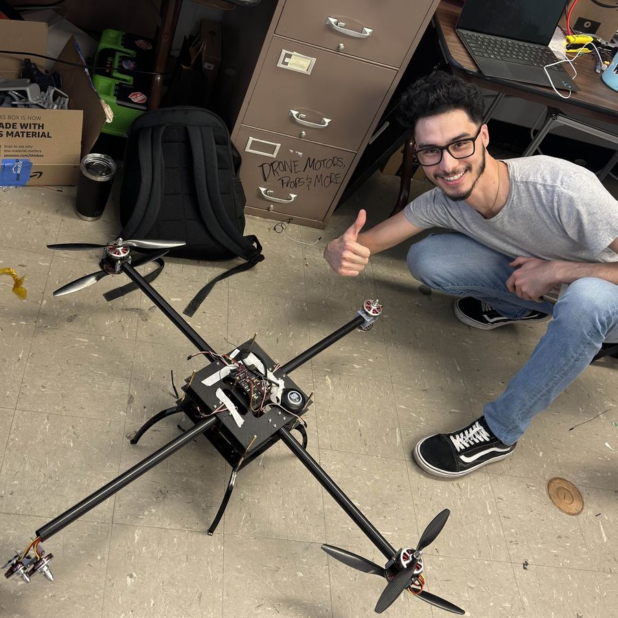 Parsa Rezaei beside the heavy-lift carrier quadcopter, showing its carbon arms, GPS module and flight controller